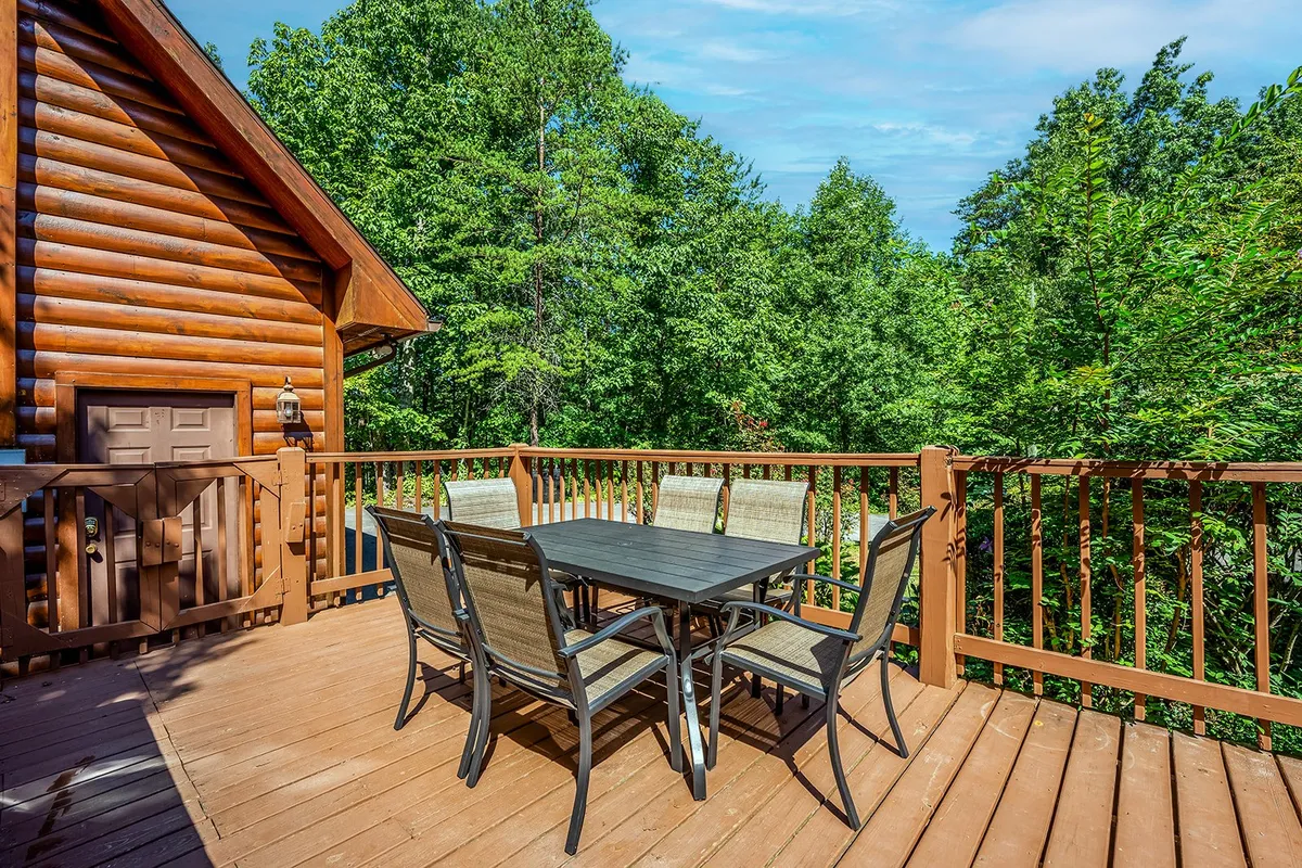 A peaceful wooden deck surrounded by trees, featuring a table and chairs perfect for outdoor dining or sipping coffee. The setting is intimate and sheltered, ideal for enjoying the sights and sounds of the mountains in any weather.