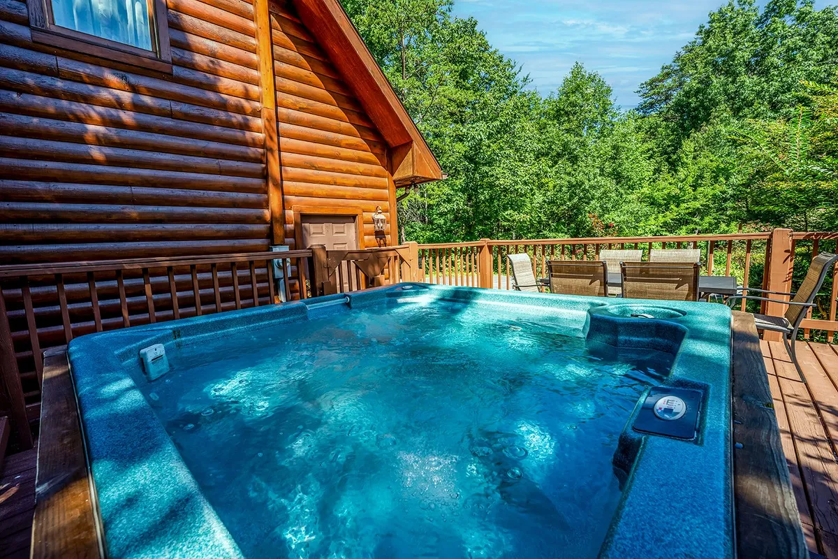 An inviting exterior view of the log cabin, featuring a private hot tub on the wooden deck, surrounded by lush trees and comfortable outdoor furniture. The scene conveys opportunities for both socializing in the hot tub and enjoying outdoor dining or gatherings amidst nature.