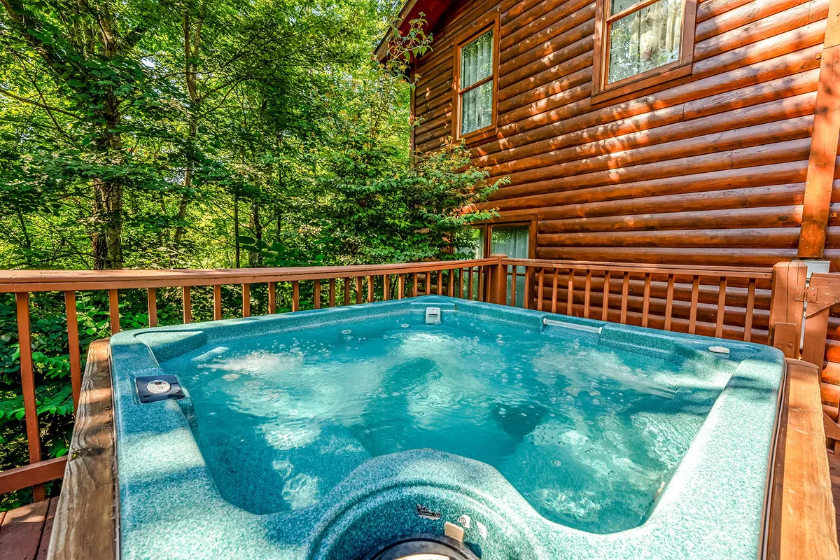 The image captures an outdoor hot tub set against the backdrop of towering trees and the rustic log cabin wall, illustrating a perfect spot for relaxation and romance. The space feels intimate and is well-suited for evening soaks under the stars or peaceful mornings.