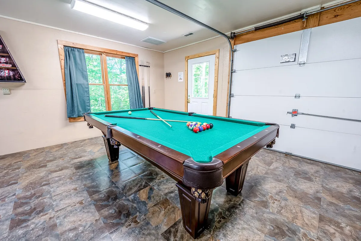 An interior shot of a game room with a pool table, windows letting in natural light, a door to the deck, and cues neatly arranged. The space invites friendly competition, socializing, and fun, all just steps from the outdoor deck.