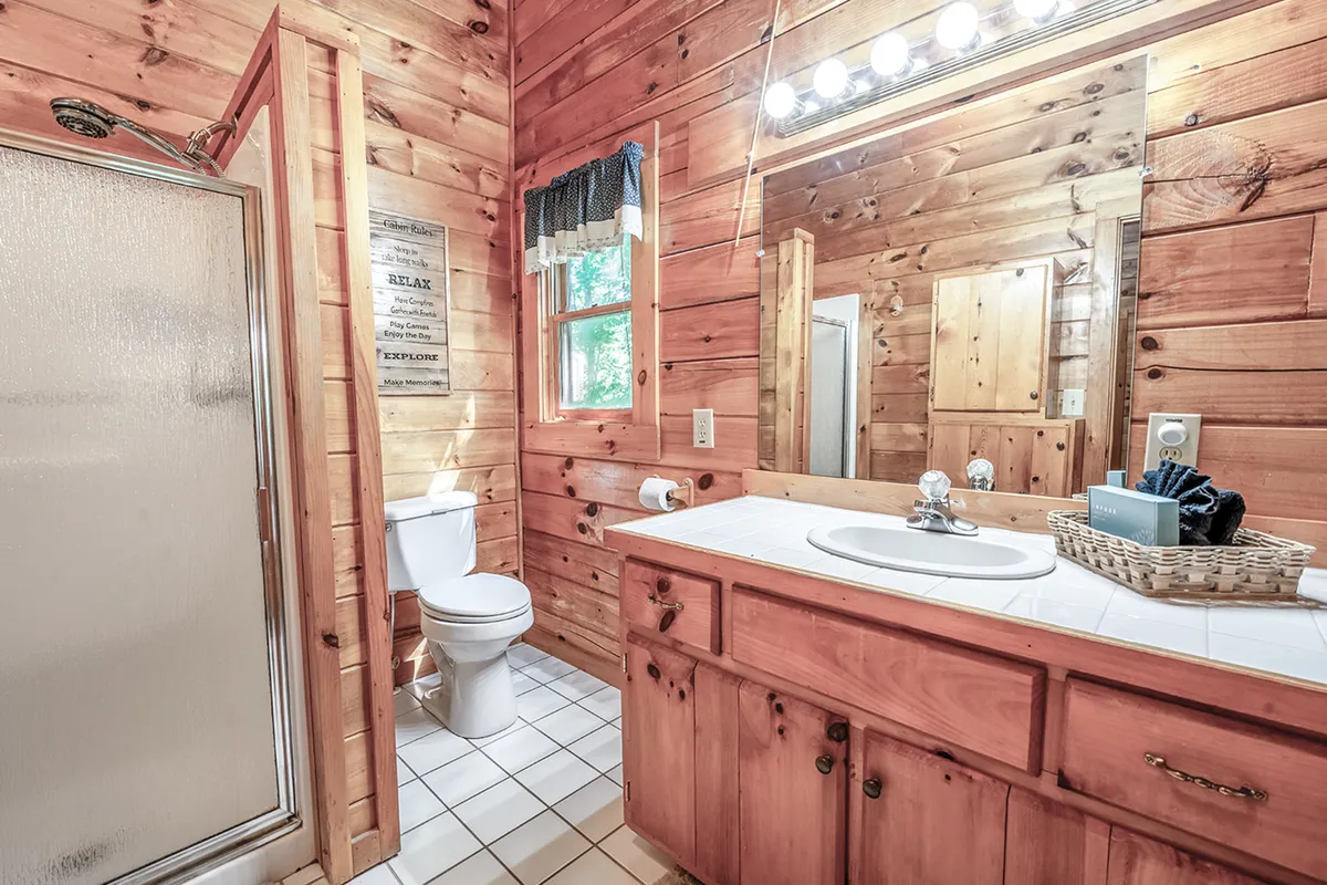 This image features a bathroom with wooden walls, a vanity with a sink, a modern shower area, and a mirror. The design is both practical and welcoming, offering a sense of privacy and relaxation for guests' daily routines.