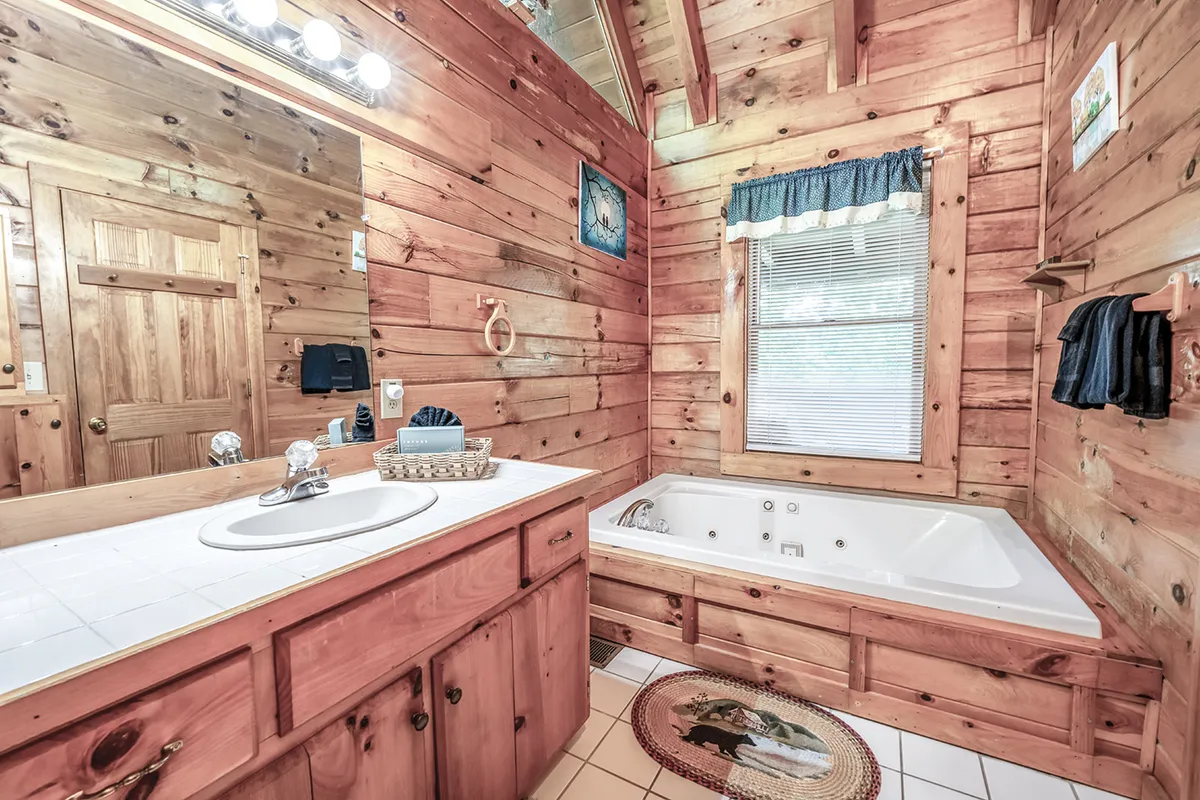 This image captures a tranquil bathroom scene featuring a luxurious jacuzzi tub, wooden walls, a vanity mirror, and a window with curtains that lets in soft natural light. The space feels both rustic and spa-like, ideal for relaxation and unwinding after a busy day.