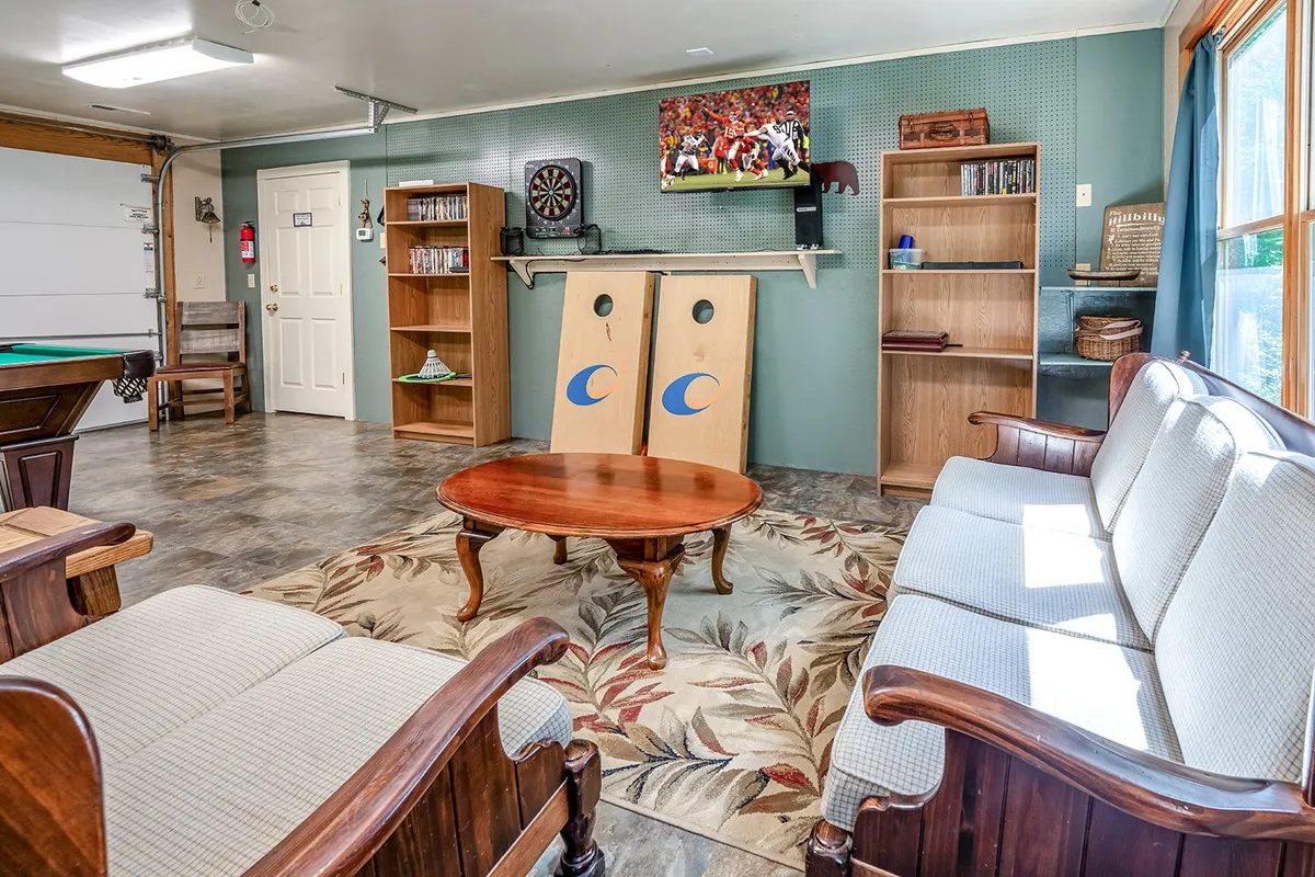 A friendly and relaxed corner of the game room featuring a dartboard, cornhole boards, cozy sofa set, coffee table, and a television. The setup encourages group fun, casual gaming, and sports viewing, supporting different entertainment styles.