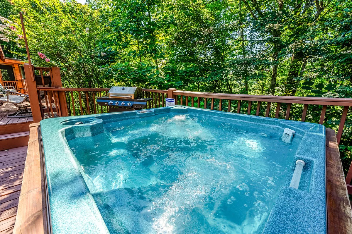 An outdoor scene showcasing a private hot tub and grill nestled among greenery. The space invites relaxation after a day of exploring, featuring both tranquil soaking and the opportunity to barbecue outdoors.